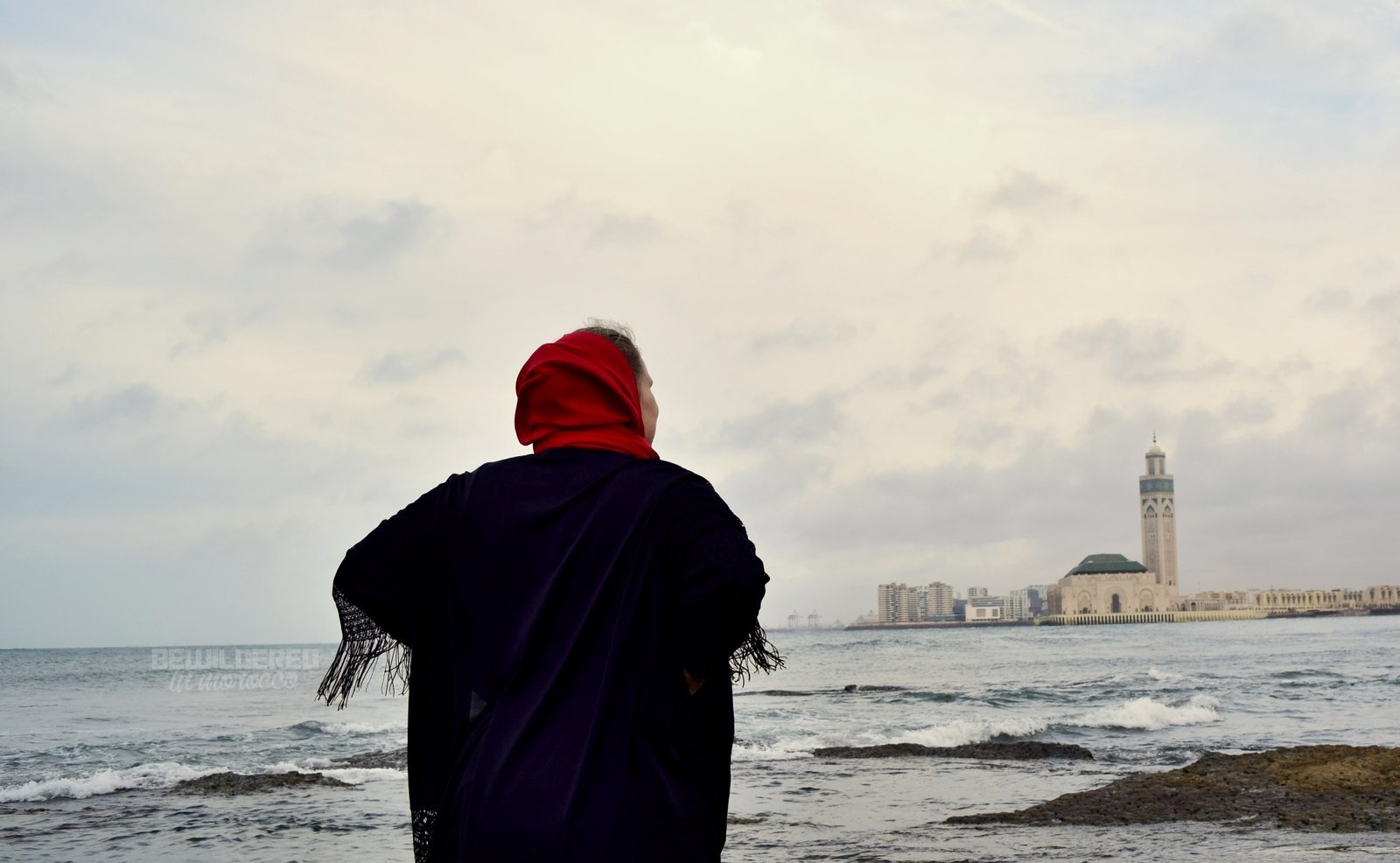 Hassan 2 Mosque, Casablanca Woman in a red headscarf looking out at the Atlantic Ocean with the Hassan II Mosque minaret in the distance, Casablanca